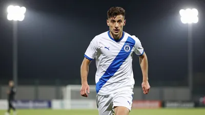 A photorealistic image of a young Dinamo Zagreb player in a white jersey with a blue stripe, running with the ball...