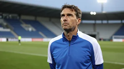 A 35-year-old Dinamo Zagreb assistant coach, wearing a plain blue and white polyester training top, stands intensely on...