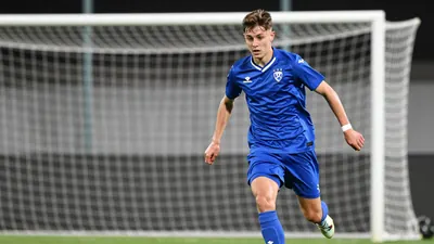 A young Dinamo Zagreb U21 player in a blue jersey, sprinting with the ball at his feet, focused on the goal ahead