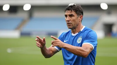 Middle-aged, muscular coach in his late 30s, short dark hair, intense eyes, wearing a plain blue training top with white...