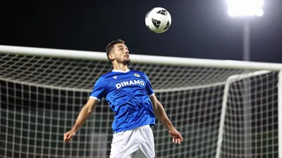 A photorealistic image of a Dinamo player in a blue jersey with white shorts, shot with a 24mm f/1.4 lens, with a shallow...