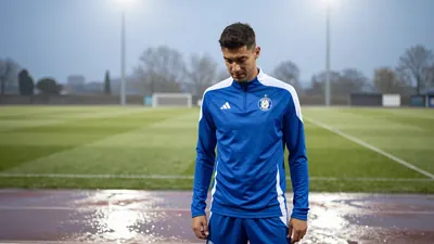 A 24-year-old Spanish defender in a plain blue and white Dinamo Zagreb training top, standing in a shallow puddle on the...