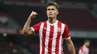 Photorealistic shot of a 24-year-old Russian midfielder in a red and white striped football kit, standing on a football...