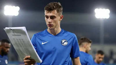 A young anonymous Dinamo Zagreb player in a solid blue kit, waist-up, focused on a tactical board, background blurred...
