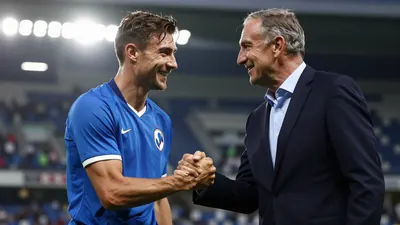 A young Croatian-American fan in a blue Dinamo Zagreb jersey, waist-up, smiling as he shakes hands with a club legend in...