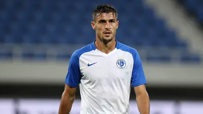 A mid-30s, athletic male Dinamo Zagreb midfielder, muscular build, waist-up, wearing a plain blue and white training top...