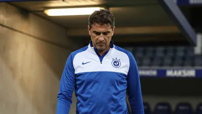 A 35-year-old Dinamo coach, stocky build, intense expression, eyes fixed on a player's tactical diagram, stands in the...