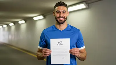 A 24-year-old athletic forward, medium-built, waist-up, smiling confidently as he holds a signed contract, wearing a...