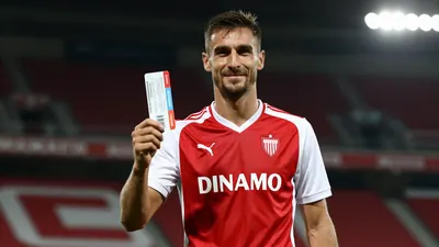 A photorealistic image of a Dinamo player in a red and white jersey, with a confident expression, holding a ticket in his...