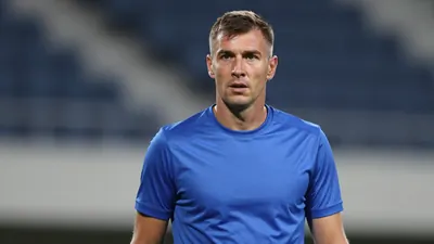 A mid-30s male club staff member in a tight waist-up shot, wearing a plain blue Dinamo Zagreb kit, focused expression...