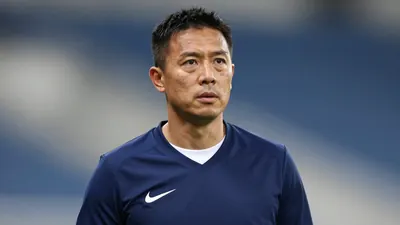 A 35-year-old male assistant coach with a rugged complexion, wearing a navy blue jersey with a smooth, unbroken fabric...