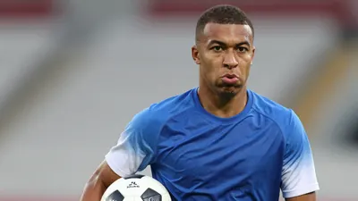 Mid-shot of a 22-year-old athletic midfielder, short dark hair, intense eyes, wearing a plain blue shirt with white...