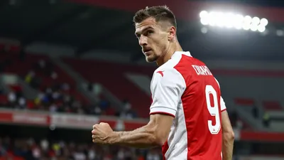 A tight waist-up shot of a Dinamo player in a red and white jersey with a white number 9 on the back, looking determined...