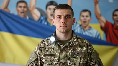 A Ukrainian soldier in a military uniform, standing in front of a large mural of Dinamo Zagreb fans, and photorealistic...