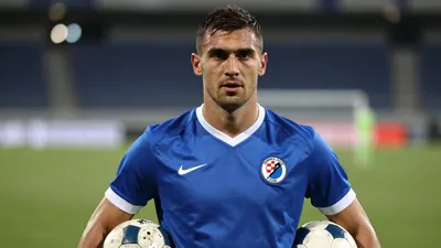 Mid-30s Croatian defender, muscular, short dark hair, intense eyes, wearing an unmarked Dinamo Zagreb home shirt - bright...
