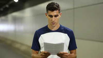 Mid-30s determined midfielder, athletic build, short dark hair, intense eyes, wearing a plain blue and white training top...