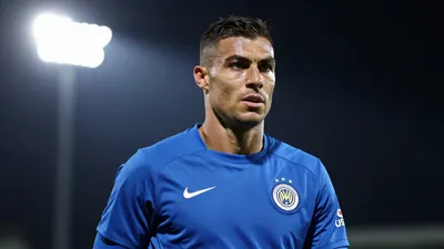 A muscular 31-year-old midfielder in a solid blue training kit, focused on his face as he looks off-camera with determination
