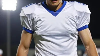 A 25-year-old male football player with a muscular build, wearing a white and blue jersey made of smooth fabric...