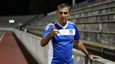 A 50-year-old male coach, 5'9" with a rugged build, stands on the tunnel wall at Stadion Maksimir, his blue and white...