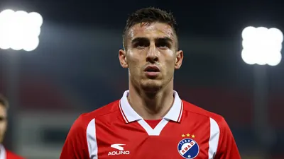 A photorealistic image of a Dinamo Zagreb player in a red and white jersey, with a determined expression, taken with a...
