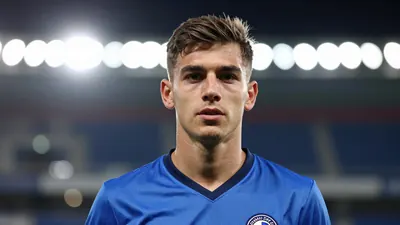 A young Dinamo Zagreb midfielder, mid-20s, wearing a solid blue kit, head-and-shoulders portrait, background blurred...