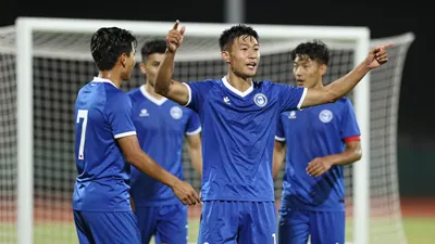 A 25-year-old male football player, wearing a blue jersey, celebrating a goal with his teammates, photographed with a...