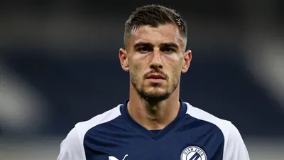 A 35-year-old defender, with a rugged build and a stern expression, wearing a Dinamo Zagreb jersey in a dark blue and...
