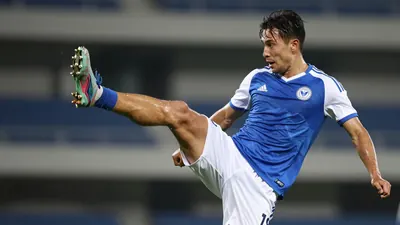 Mid-20s male forward, athletic build, hair damp, eyes focused, mid-air executing a scissors-kick, blue jersey with white...