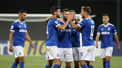 A photograph of Dinamo players celebrating a goal with Thun player in the background, looking disappointed, taken during...