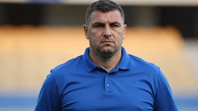 Photorealistic close-up of a broad-shouldered male GNK Dinamo Zagreb staff member in his mid-30s, wearing a solid blue...