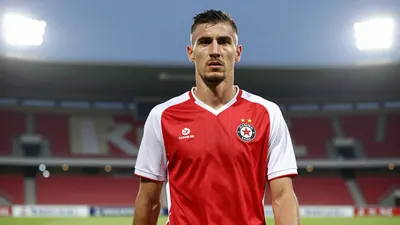 A photorealistic image of a Dinamo Zagreb player in a red and white jersey, with a serious expression, standing in front...