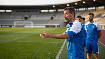 A 35-year-old, ruggedly-built coach, clad in a plain blue and white polyester training top, stands intensely on the edge...