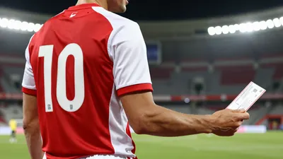 A photorealistic image of an anonymous Dinamo player in a red and white jersey, with a number 10 on the back, holding a...