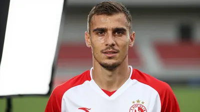 A photorealistic image of an anonymous Dinamo player in his mid-20s, with a strong build, wearing a red and white jersey...