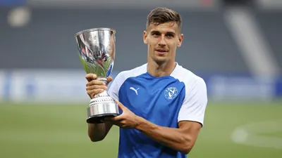 A mid-20s, athletic-built Dinamo Zagreb player, waist-up, face bright and focused, wearing a plain blue and white...