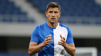 Mid-40s male coach, athletic build, waist-up, intense expression, plain unmarked training top split blue left side, white...