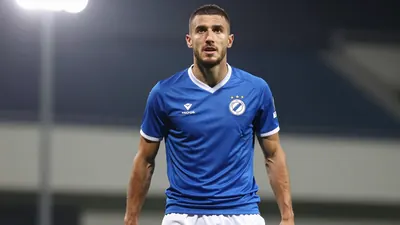 A tight, waist-up shot of an anonymous Dinamo Zagreb player in a blue jersey with white shorts, looking focused and...