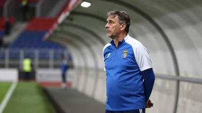 A 50-year-old, ruggedly-built, assistant coach of Dinamo Zagreb, wearing a plain blue and white polyester training top...