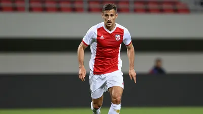 A tight action crop of a Dinamo player in a red and white jersey, with a white kit and a black and white ball, running...