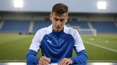 Medium shot of a young Dinamo Zagreb player in a plain blue and white training top, standing pitchside at Stadion Maksimir