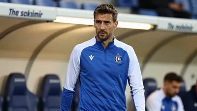 A concerned, athletic-built GNK Dinamo Zagreb midfielder in his mid-30s, wearing a plain blue and white training top...